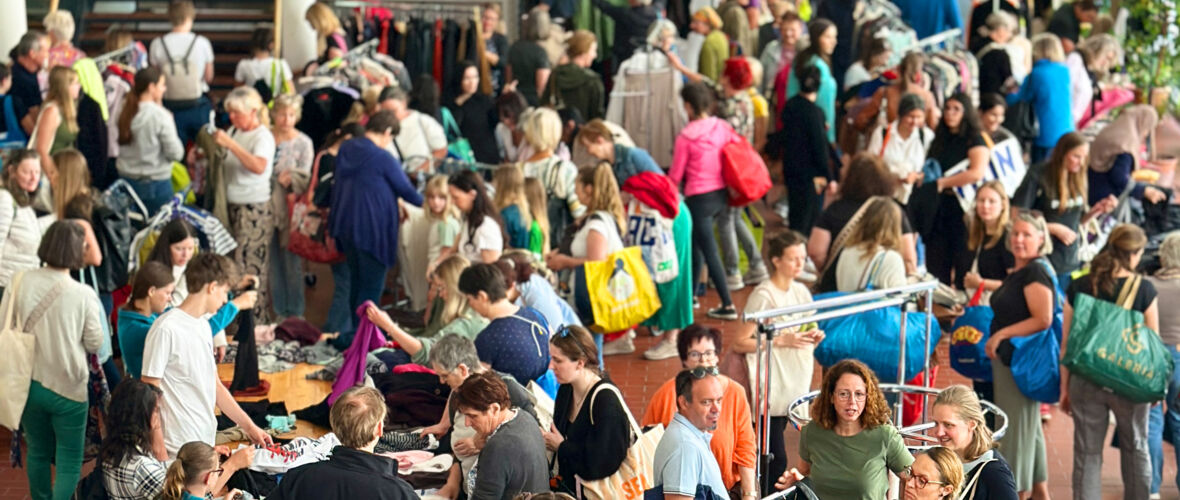 Flohmarkt mit vielen Menschen, die Kleidung und Taschen durchsuchen