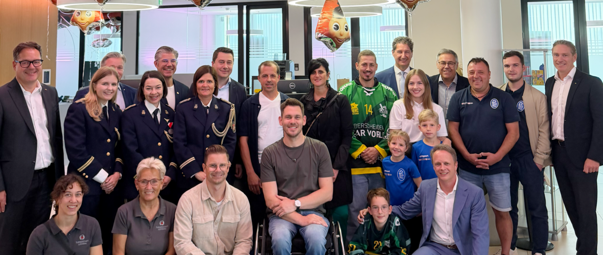 Gruppe von Personen, darunter ein Eishockeyspieler in Uniform und zwei Frauen in Uniformen, posieren für ein Foto.