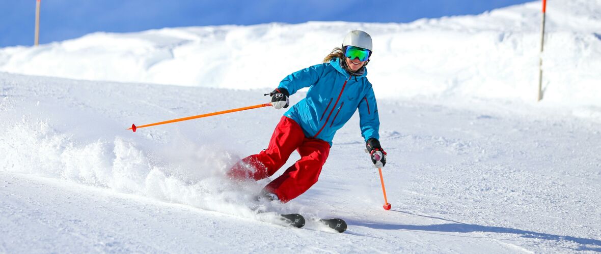 Skifahrerin in blauer Jacke und roter Hose fährt auf verschneiter Piste im Schnee auf einem Skigebiet in Österreich.