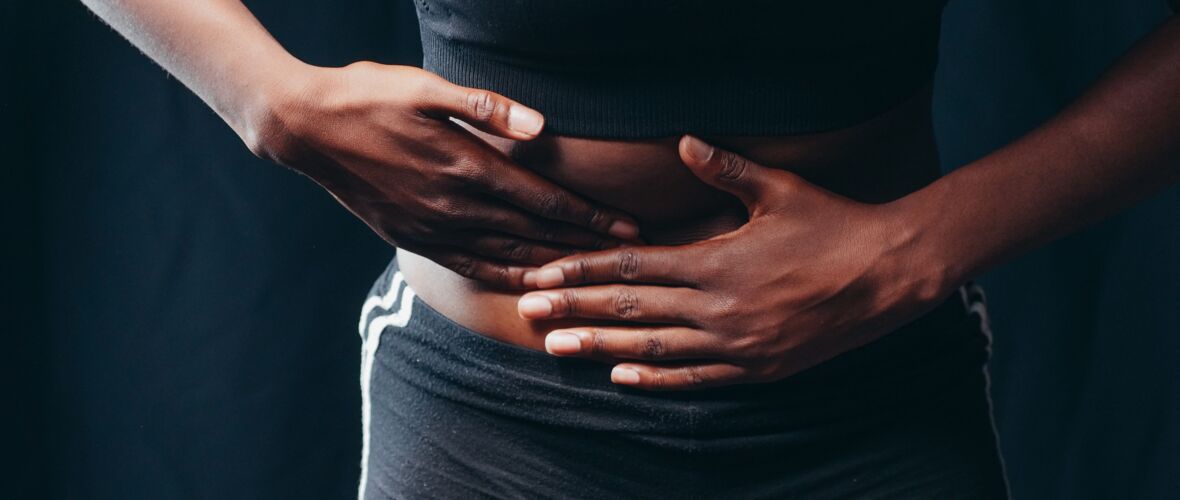 Frau mit Händen auf dem Bauch, dunkler Hintergrund.